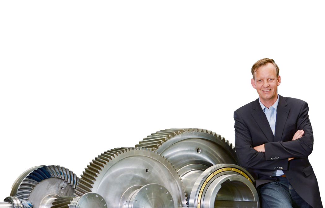 Der Geschäftsführer Herr Alexander Kachelmann von Colberg der Firma KACHELMANN GETRIEBE GmbH lehnt auf der rechten Seite an einem Getriebe, während er in die Kamera lächelt. KACHELMANN GETRIEBE GmbH